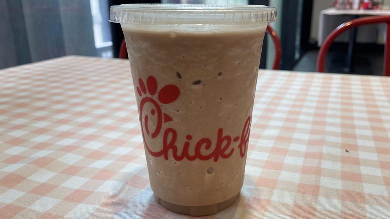 A blended S'mores Frosted Coffee in a Chick-fil-A plastic cup sits on a checkered tablecloth.