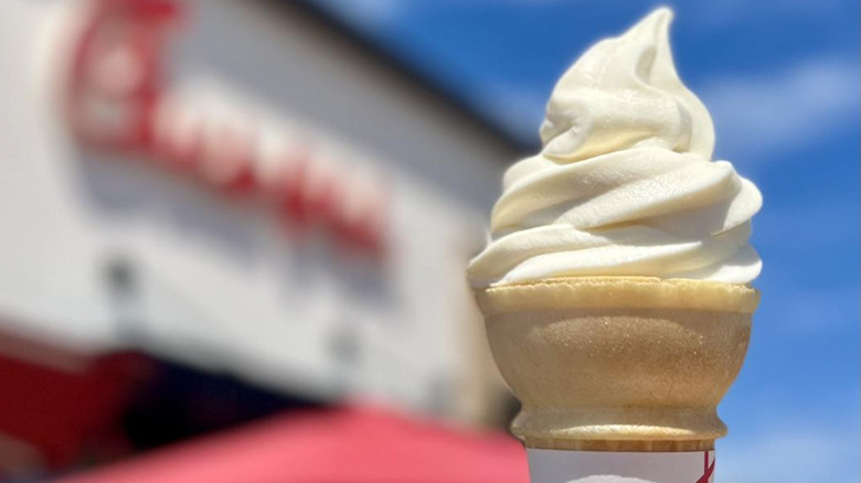 Someone holds a Chick-fil-A vanilla icedream scoop on a cone in front of a blurred Chick-fil-A logo
