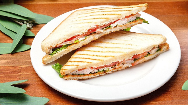 Chicken Caesar salad sandwich on white bread cut in half on a white plate