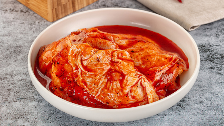 Raw chicken thighs marinating in a white bowl sitting on counter.