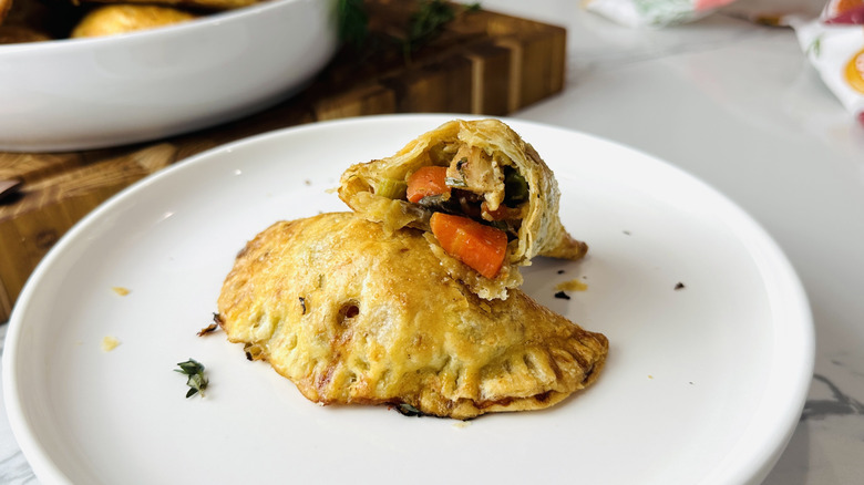 small semicircular baked pies on a white plate; one is broken open