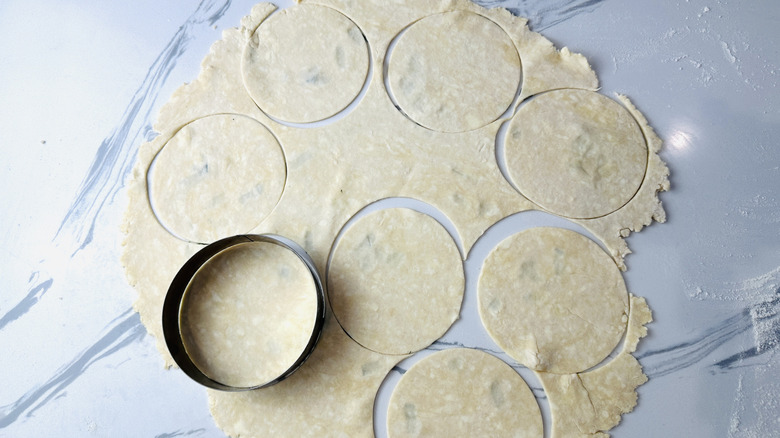 flattened dough on a kitchen counter with circular impressions and a round cookie cutter