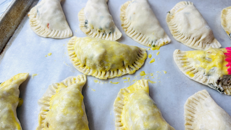 small semicircular unbaked pies partially covered in raw egg