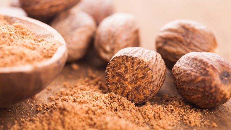 Whole and ground nutmeg with a wooden spoon.