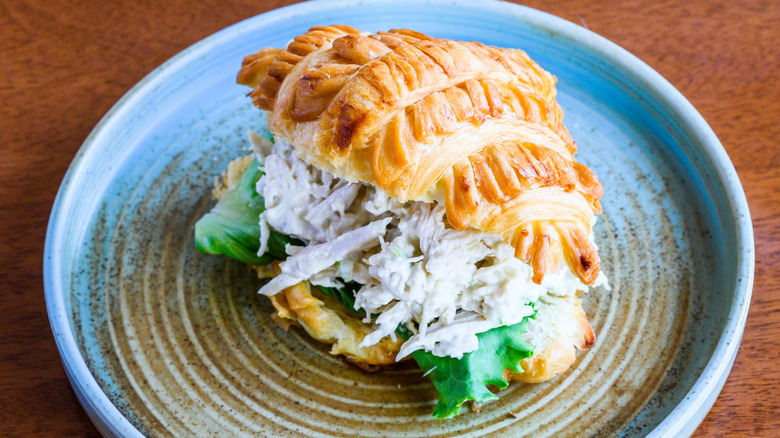 A butter croissant filled with creamy chicken salad on top of a plate
