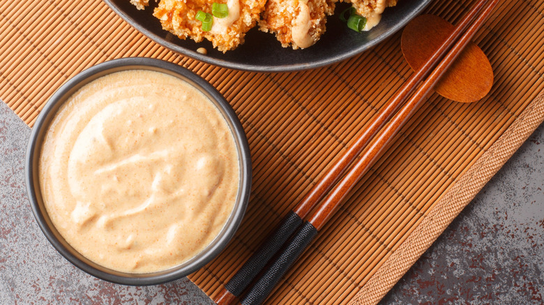 Bang bang sauce in a bowl with chopsticks on the side, all on a bamboo mat