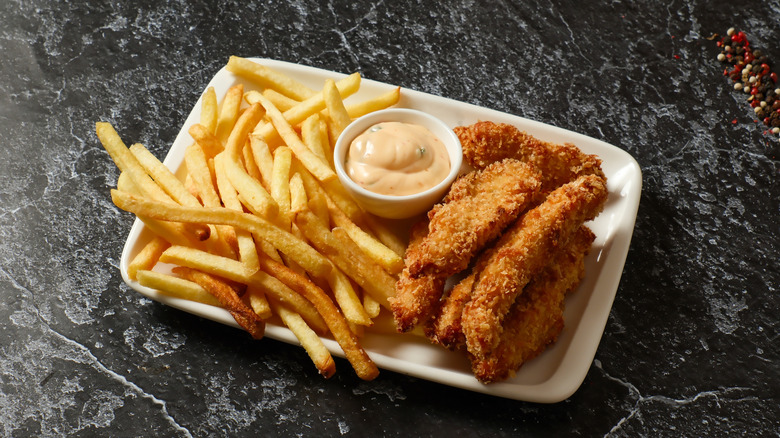 Chicken tenders and fries on a plate with a side dipping sauce.
