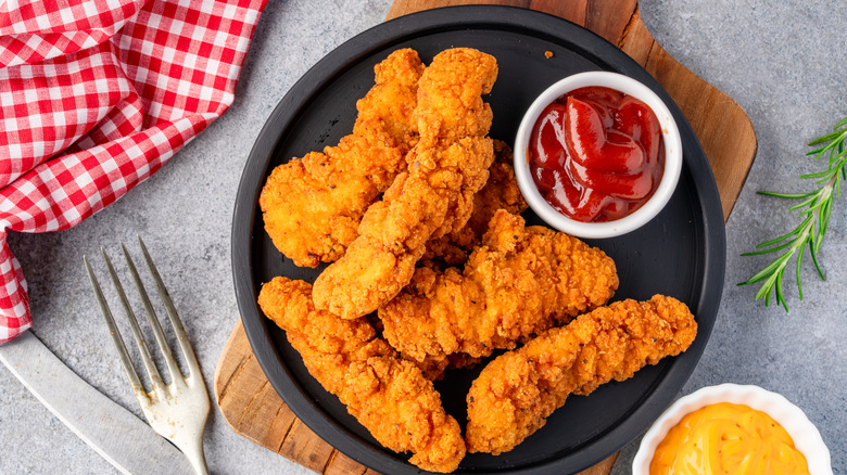 Chicken tenders on a plate with a side of ketchup and mustard.