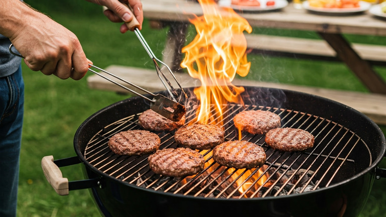 A person's hands are seen grilling burgers outdoors.