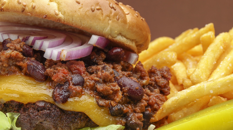 A chili cheese burger is photographed in close-up with a side of fries.