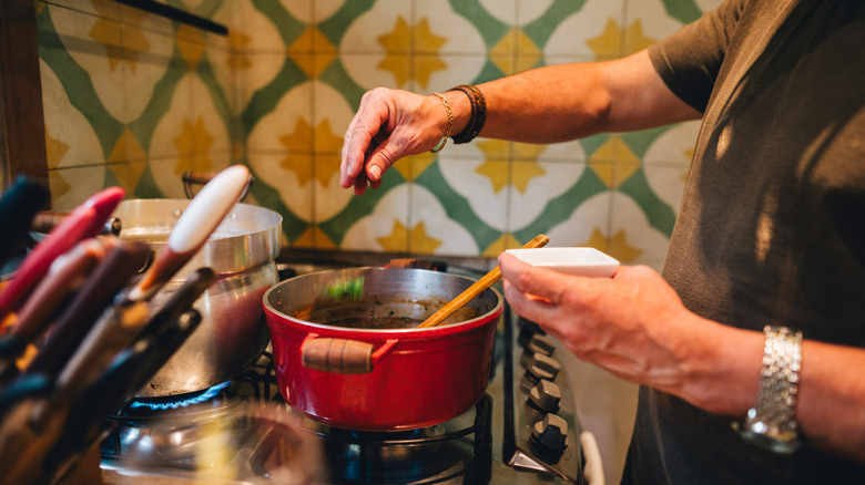 Person adding seasoning to a pot of chili on the stovetop