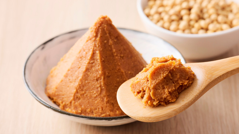 A spoon full of miso paste hovers over a full bowl.