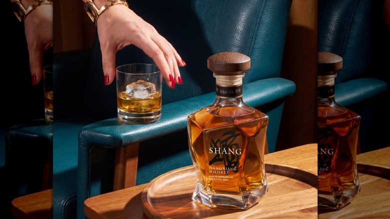 Hand reaching for a glass of Shāng Whiskey with a bottle of Dàn Yă  in foreground