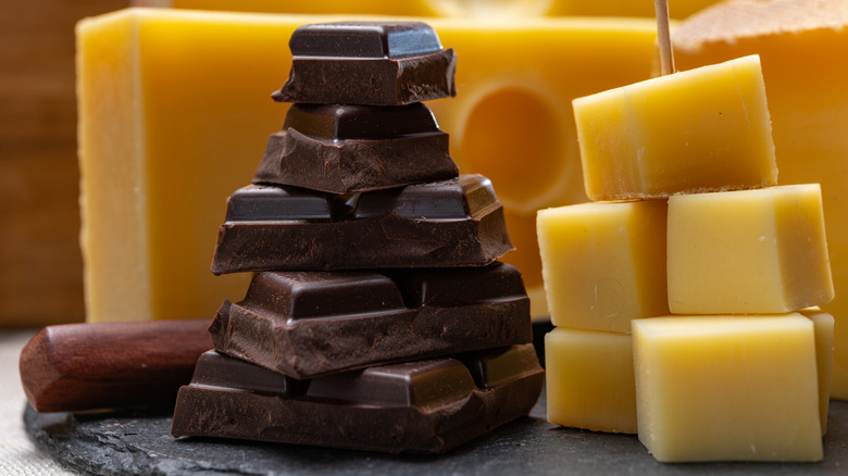 a block of cheese sits next to a stack of broken chocolate bars
