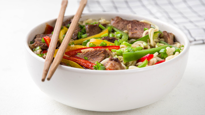 bowl filled with beef lo mein noodles and a pair of chopsticks