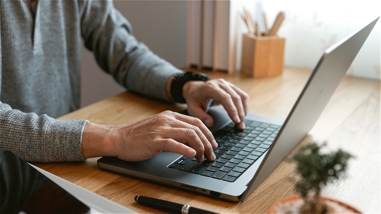 A person with hands on laptop on desk with office supplies
