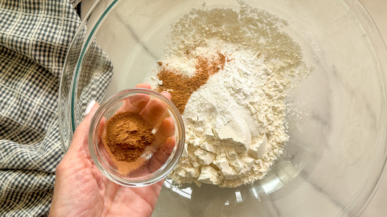 hand adding cinnamon to bowl with flour