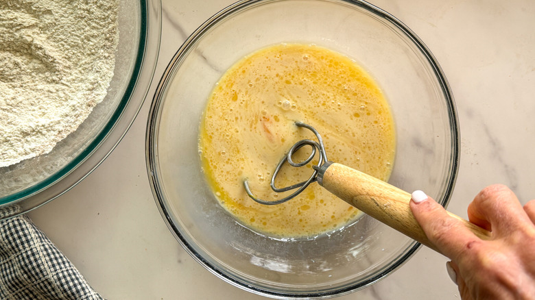 Hand using whisk to mix eggs in bowl