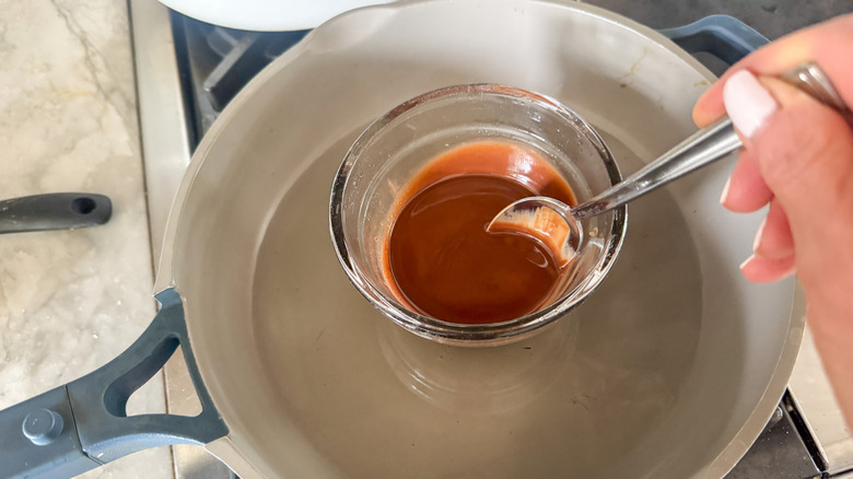 hand stirring chocolate in small bowl in pan