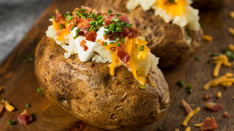A baked potato topped with sour cream, shredded cheese, bacon, and chopped chives