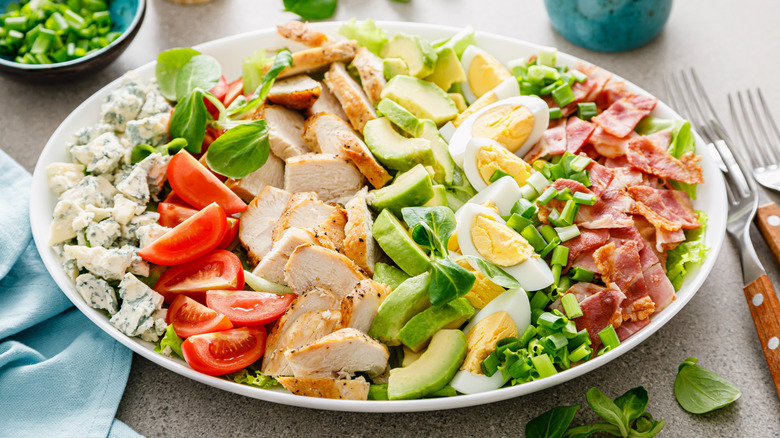 Cobb salad with rows of blue cheese, tomatoes, chicken, avocado, hardboiled eggs, and bacon