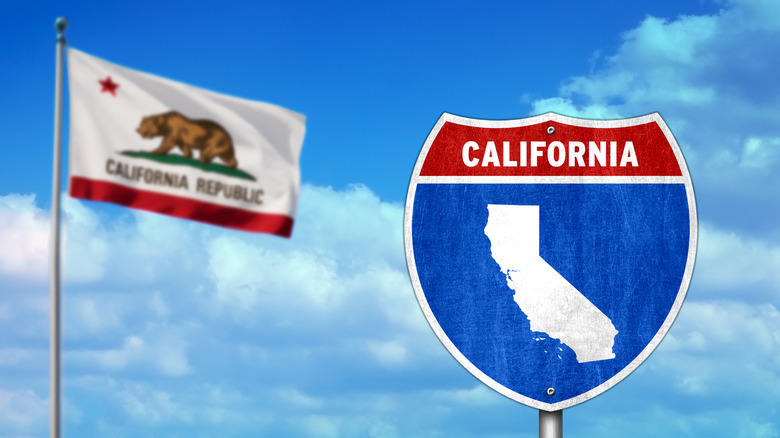 California road sign and California flag against blue sky and clouds