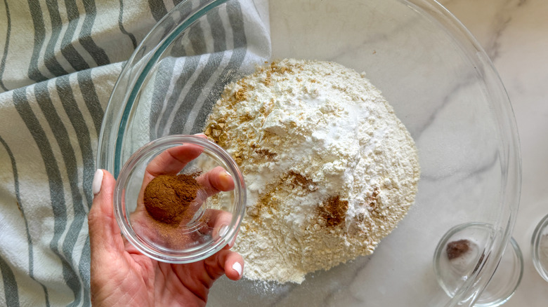 Hand adding cinnamon to bowl with flour and other spices