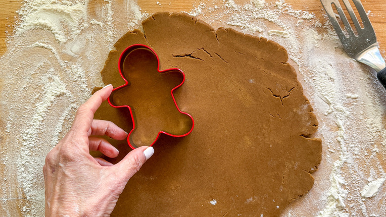 Hand pressing gingerbread man cookie cutter into dough