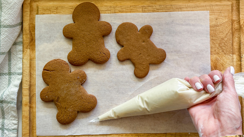 Hand holding piping bag with icing next to gingerbread men cookies