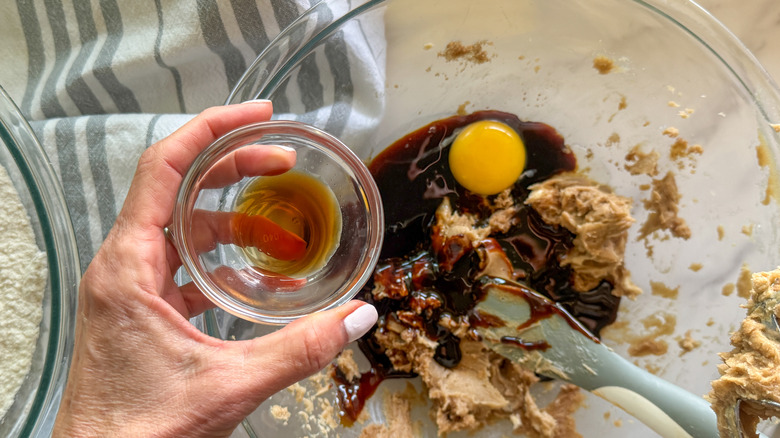 Hand adding vanilla to bowl with egg and molasses