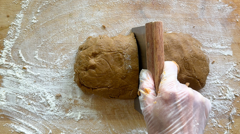 Hand cutting gingerbread cookie dough in half with bench scraper