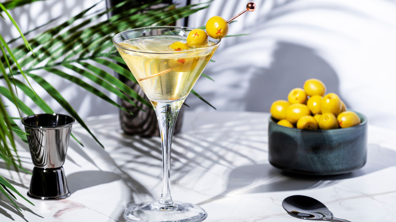 A dirty martini in a V-shaped cocktail glass beside a bowl of olives.
