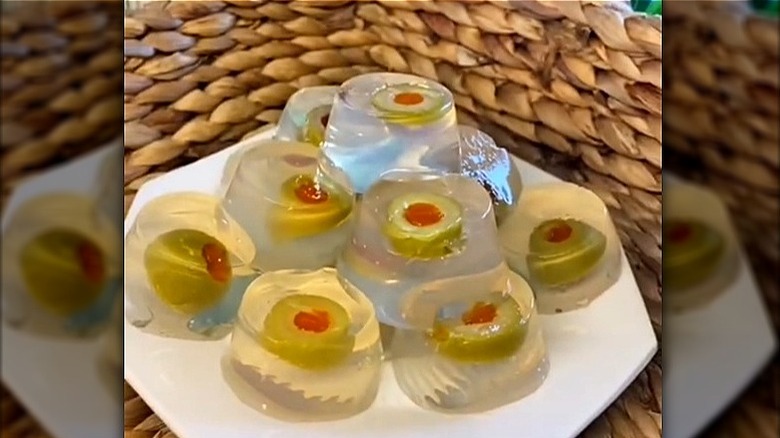White plate of dirty martini Jell-O shots with slices of green olives.