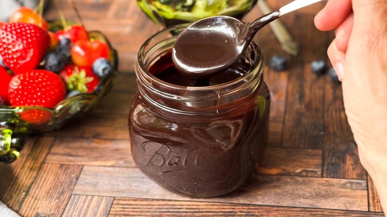 Classic hot fudge sauce on spoon and in jar with berries