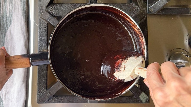 Stirring classic hot fudge sauce in saucepan on stovetop with wooden spoon