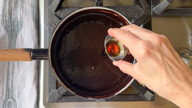 Pouring vanilla extract into classic hot fudge sauce in saucepan on stovetop
