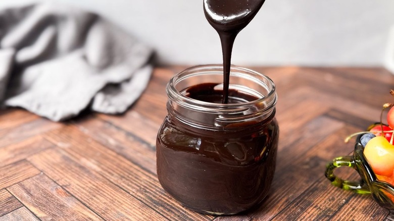 Classic hot fudge sauce dripping from spoon into glass jar