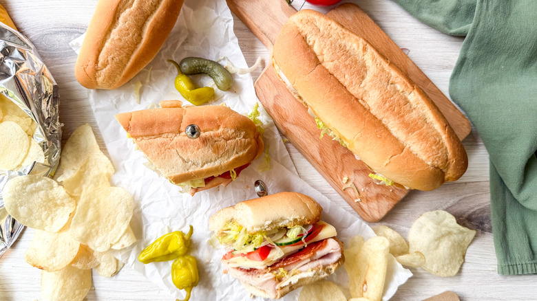 Classic Italian-ish club sub sandwich on cutting board and sliced with potato chips and peppers