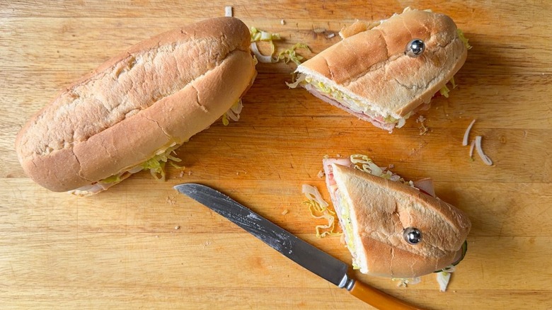 Sliced and whole classic Italian-ish club sub sandwiches on cutting board with knife and sandwich picks