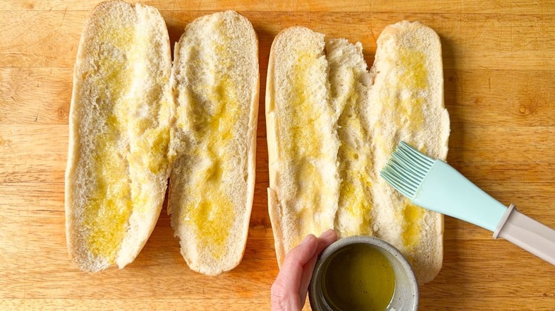 Brushing olive oil onto cut Italian rolls with pastry brush