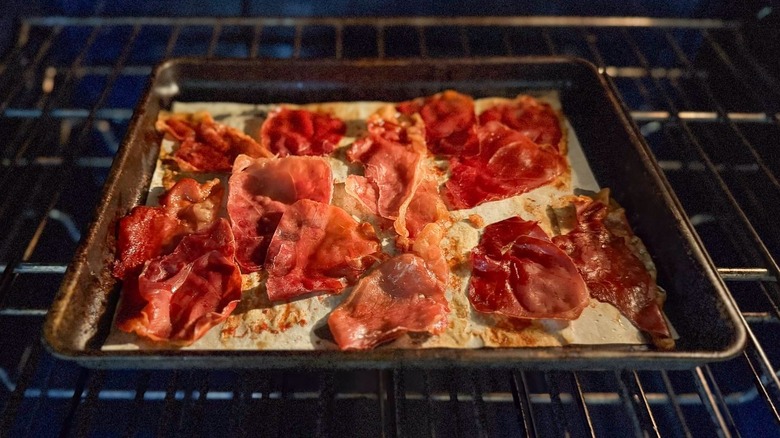 Crispy prosciutto slices on parchment-lined baking sheet in oven