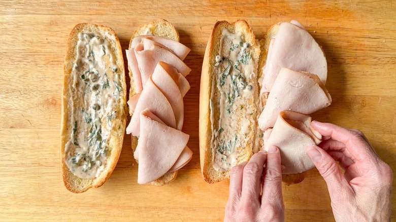 Laying folded smoked turkey slices on sliced and dressed Italian rolls