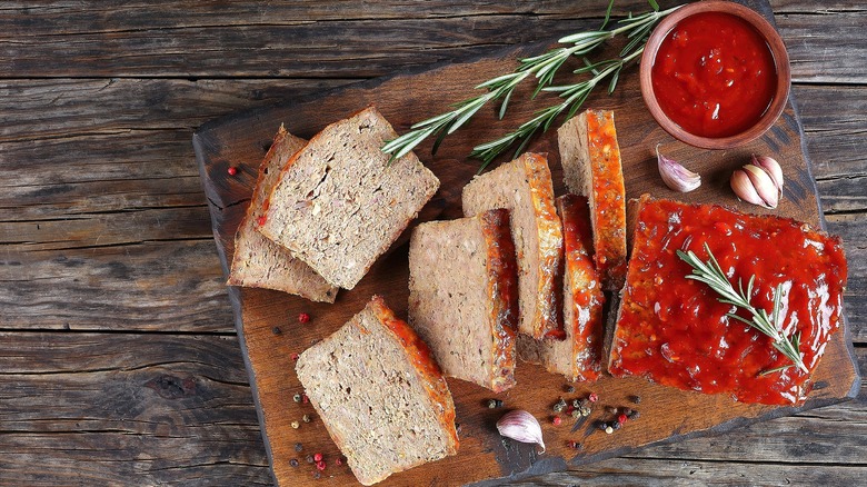 Top-down view of sliced meatloaf and sprigs of rosemary on a wooden cutting board