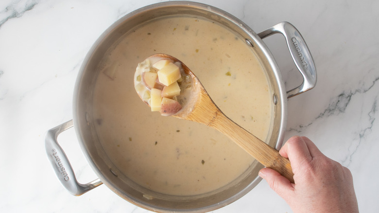 hand holding a spoonful of potatoes over a pot of pinkish liquid