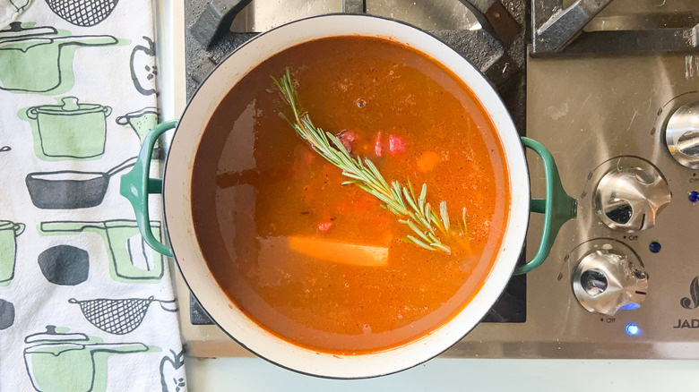 Rosemary sprig and parmesan rind in tomato broth in pot on stove