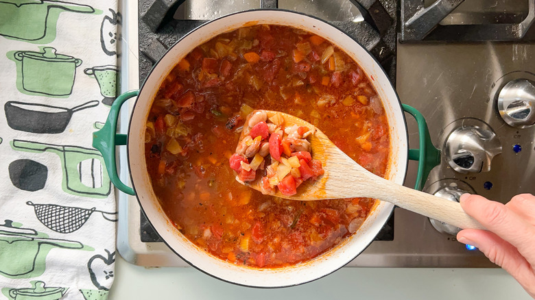 Adding beans and pancetta to soup pot on stove