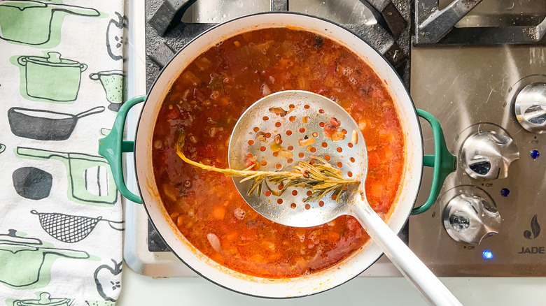 Removing rosemary sprig from soup pot with slotted spoon