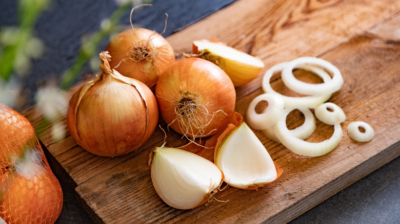 Whole and sliced onions are arranged on a cutting board.