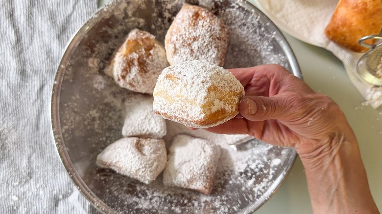 Holding a classic sugar-coated beignet over a bowl of beignets