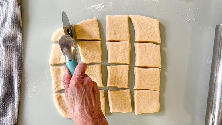 Using a pizza cutter to cut rolled out beignet dough into squares